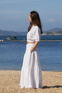 Model side profile wearing high-waisted tiered maxi skirt in white on beach