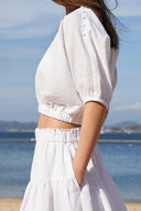 Model wearing high-waisted tiered maxi skirt in white on beach, side profile of waistband