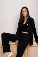 Model wearing wide leg pants in black paired with cardigan sitting on ledge