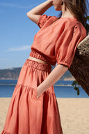 Model wearing high-waisted tiered maxi skirt in terracotta on beach, close up of waistband and pocket