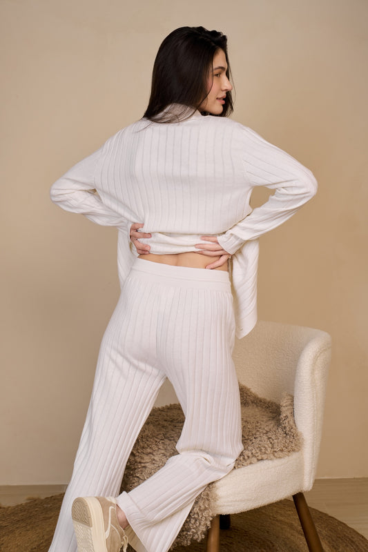 Back view of model wearing long cardigan in white swan paired with wide leg pants leaning against chair