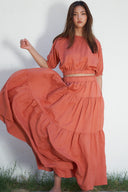 Model wearing high-waisted tiered maxi skirt in terracotta, full profile