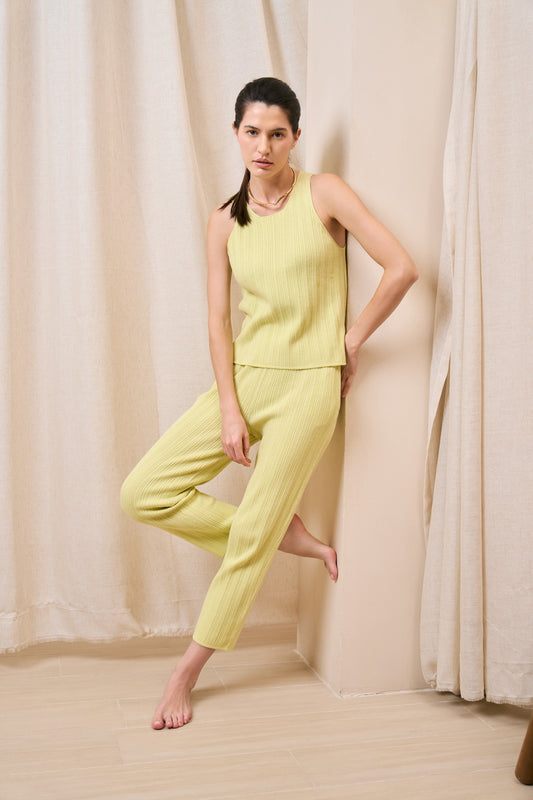 Model wearing ribbed tank in lemon mousse paired with tapered pants against wall